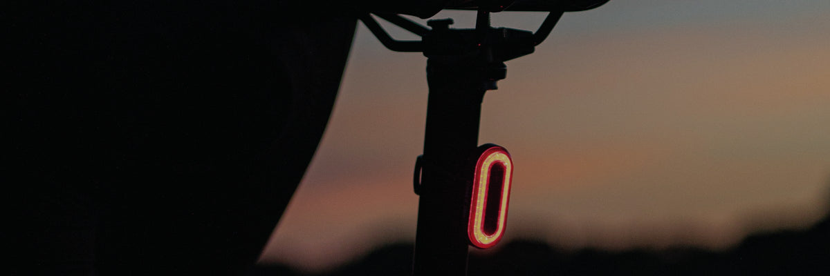 Feu arrière vélo KHEAX allumé sur la tige de selle au coucher du soleil