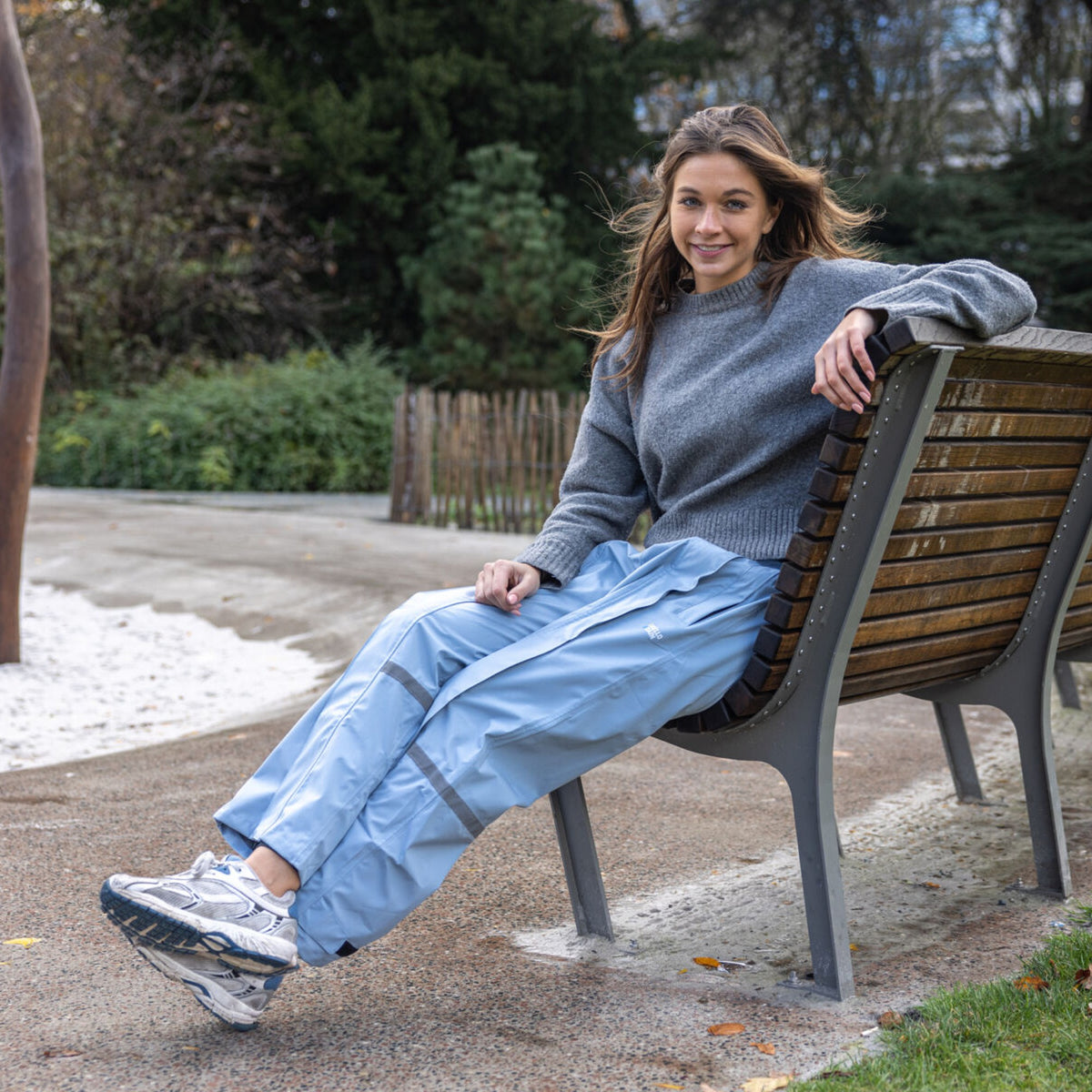 Femme assise sur un banc en pantalon de pluie Hello Rain bleu clair