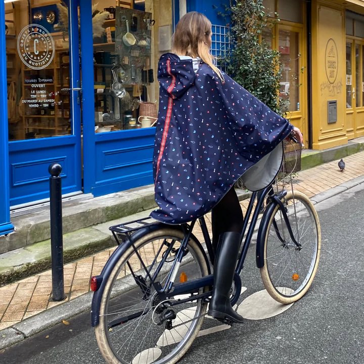 Cycliste en cape de pluie bleu marine sur un velo de ville dans une rue mouillee