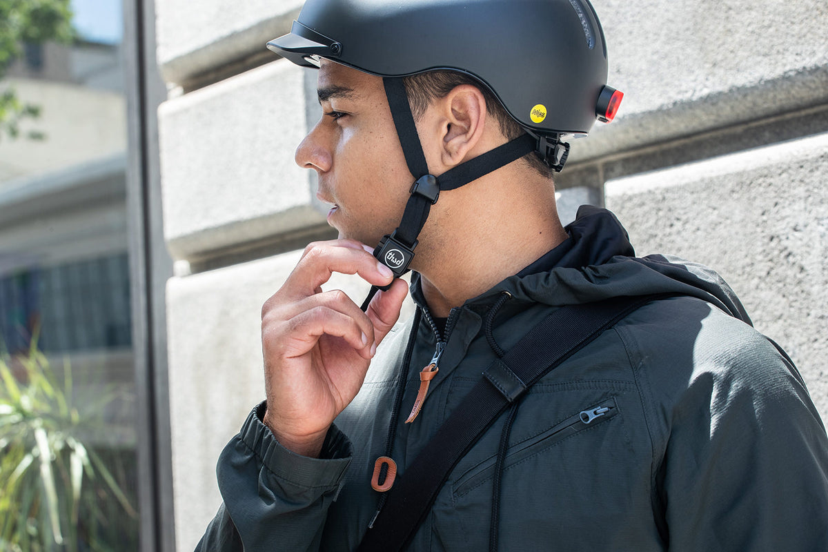 Cycliste urbain ajustant la jugulaire de son casque devant un immeuble